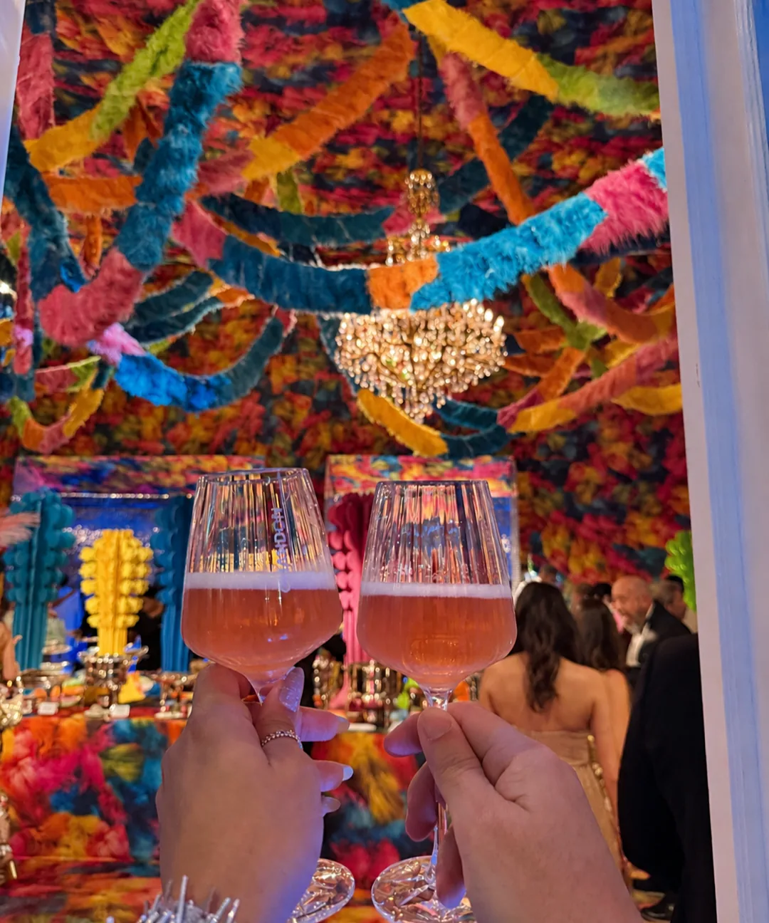 Des invités portant un toast au champagne sous un lustre et une décoration à franges colorées lors du Copa Ball.